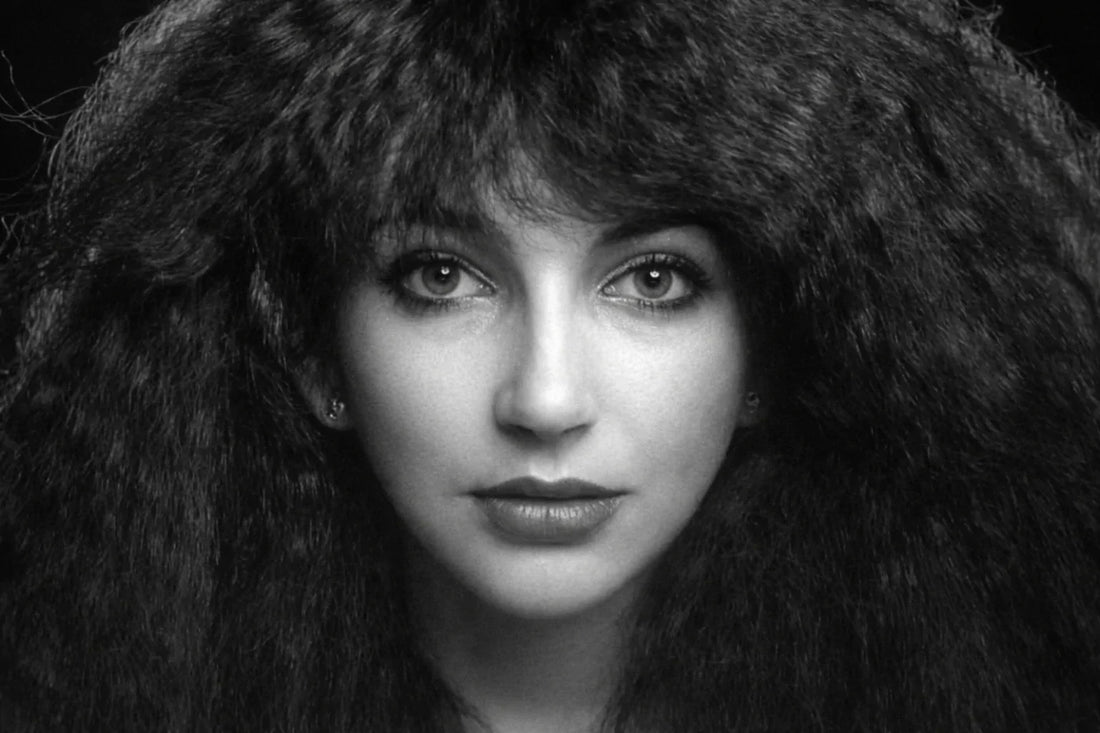 Black-and-white close-up portrait of a female singer with voluminous, curly hair framing her face, looking directly at the camera with a calm, intense expression. Soft lighting highlights her eyes and lips against a dark background.
