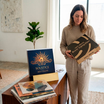 Woman unboxing Vinyl Break record display stand with gold finish and Now Playing slot on credenza