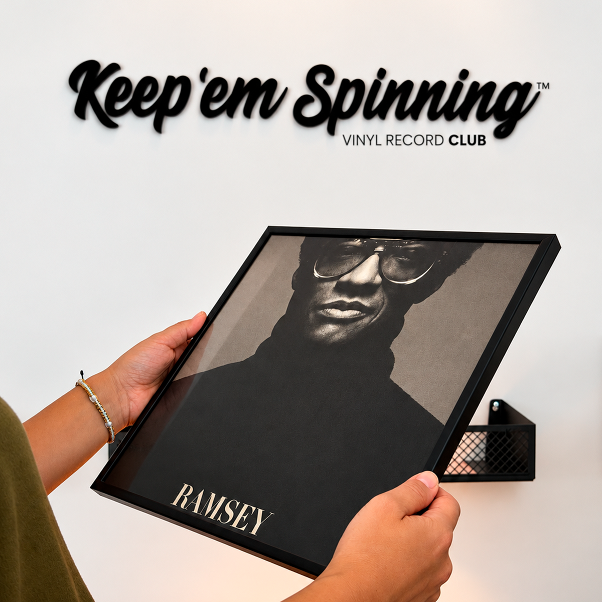 Hands holding the black 12" vinyl record frame in front of the Keep 'em Spinning logo