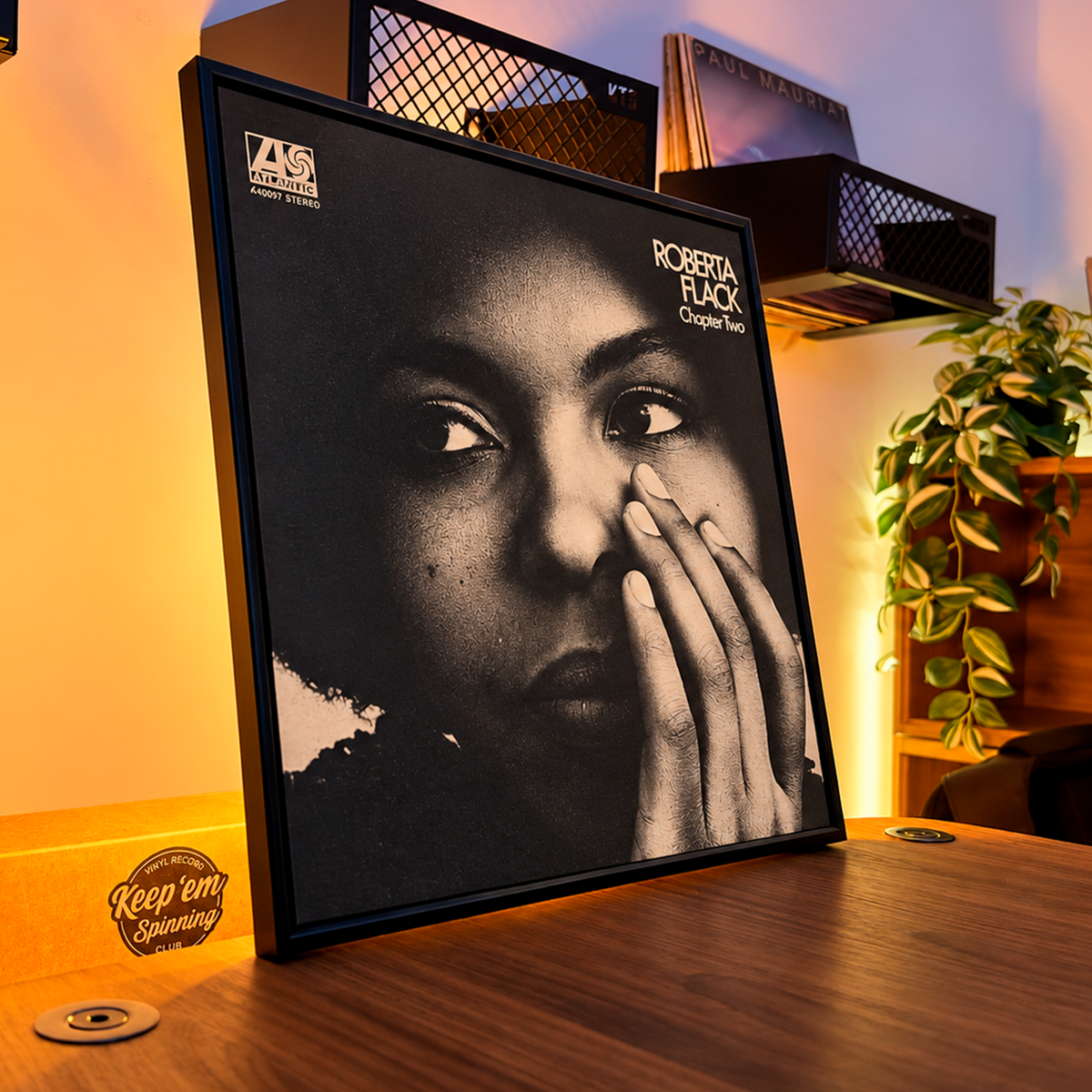 Black 12" vinyl record frame leaning on a desk, showing an album cover in warm light